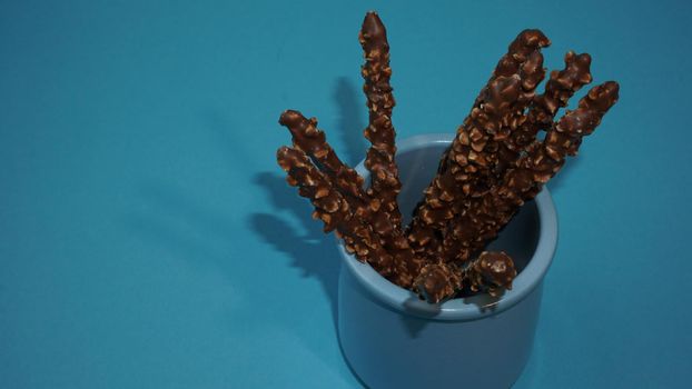 Chocolate crispy sticks with hazelnut sprinkles on a blue background.