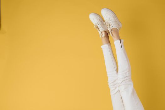 Female legs white jeans sneakers fashion yellow background view. High quality photo