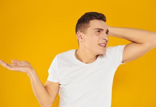 A guy in a white T-shirt spreads his arms to the sides on a yellow background emotions model. High quality photo