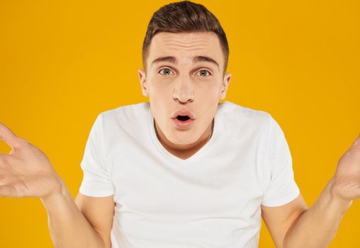 A guy in a white T-shirt spreads his arms to the sides on a yellow background emotions model. High quality photo