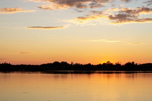 Colorful sunny sunset on a calm lake. The sun is reflected on the surface of the water.