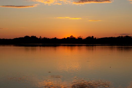 Colorful sunny sunset on a calm lake. The sun is reflected on the surface of the water.