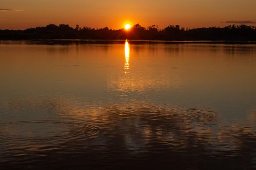 Colorful sunny sunset on a calm lake. The sun is reflected on the surface of the water.