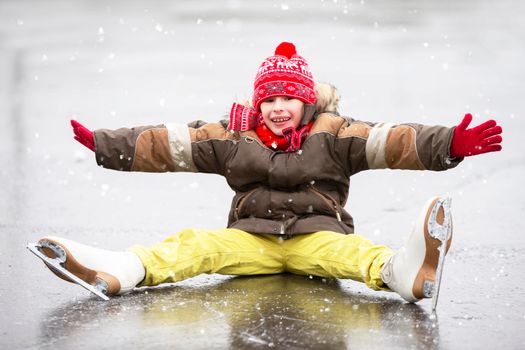 Little joyful boy fell down while skating. The child is skating on ice in the winter.