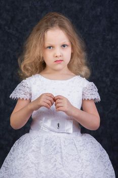 Cute little blonde girl in a beautiful white dress on a dark background. Six year old beautiful girl