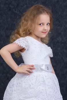 Cute little blonde girl in a beautiful white dress on a dark background. Six year old beautiful girl