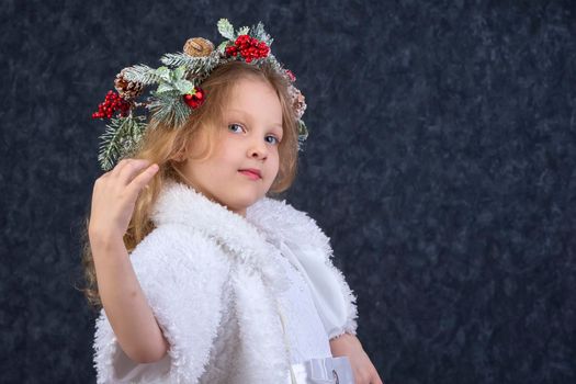 Beautiful little girl in a white dress with a Christmas wreath on her head. Christmas child.