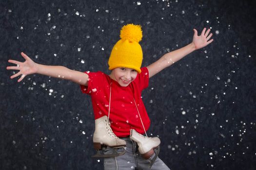 Handsome little boy in a knitted yellow hat with vintage skates on a gray background.