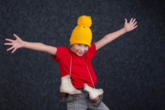 Handsome little boy in a knitted yellow hat with vintage skates on a gray background.