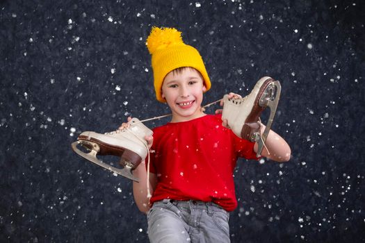 Handsome little boy in a knitted yellow hat with vintage skates on a gray background.