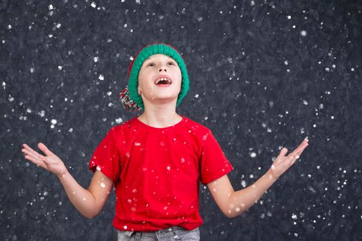 A funny little boy in a red T-shirt catches the flying snow.