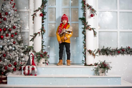 Handsome little boy in christmas. Funny child holds old skates and stands on the porch of a house decorated with Christmas tree decorations
