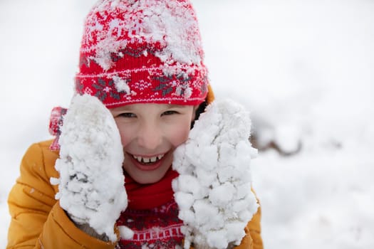 Happy little boy in winter in snow-covered mittens.