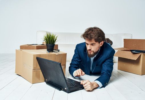 A business man lies on the floor in front of a laptop, work with no unpacked things. High quality photo