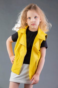 Beautiful little blonde girl in a yellow jacket on a gray background. Five year old girl. Model tests for a child.