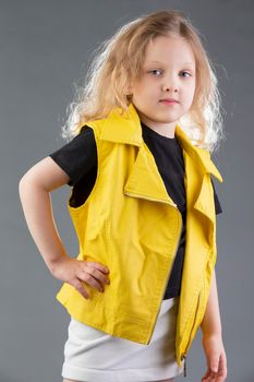 Beautiful little blonde girl in a yellow jacket on a gray background. Five year old girl. Model tests for a child.