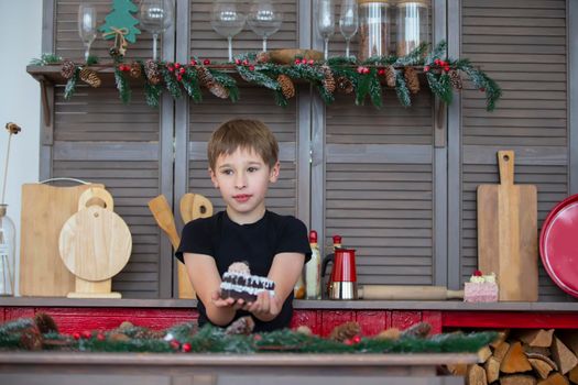 A boy in the Christmas kitchen at home holds a cake in his hands.