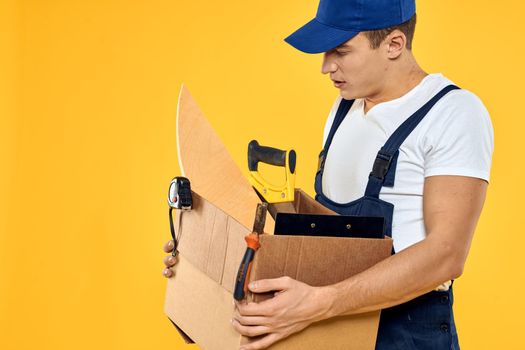 A man with a box in his hands working uniform that delivery service yellow background. High quality photo