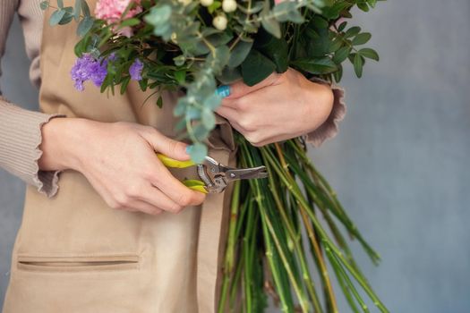 Florist cuts the stems of flowers in a bouquet with a secateurs. People in the process of work. The concept of a flower shop and flower delivery as a family business.