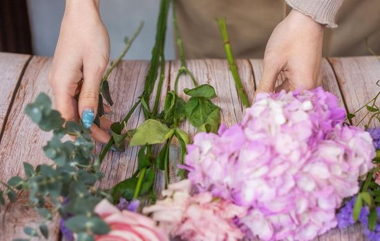 Florist at work. Female hands collect a romantic bouquet of roses. People in the process of work. The concept of a flower shop and flower delivery as a family business.