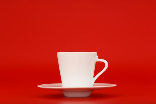 White porcelain coffee cup on saucer against red background with copy space. Minimalistic still life with coffee against red background. Concept of energy drinks