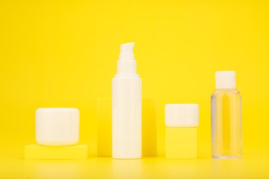 Set of cosmetic bottles with yellow geometric props against bright yellow background. Concept of skin care and protection during summer