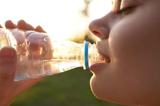 woman drinks water from a plastic bottle outdoors in summer close-up. High quality photo