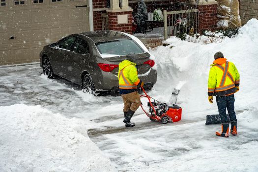 After a night storm, workers clear snow from the entrance to the garage