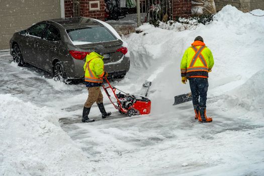 After a night storm, workers clear snow from the entrance to the garage