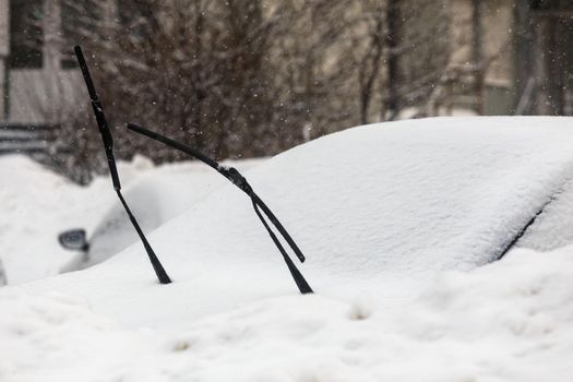 wipers sticking out of the snow coverd car at cloudy day light, telephoto shot with blurry background