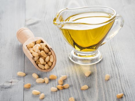 Pine nut oil and pine nuts in wooden scoop on gray wooden background