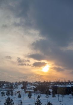 The sun among the clouds over the winter city. Beautiful background. The sky and clouds are painted in different colors.