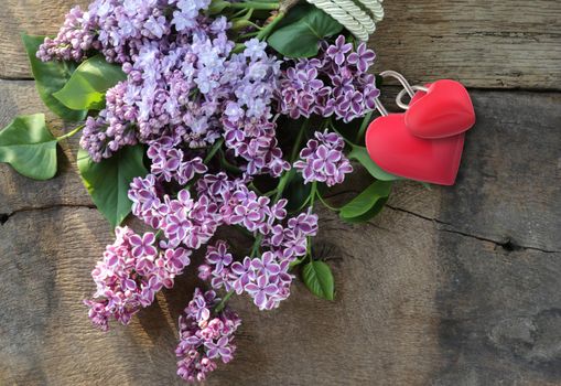 Beautiful spring flowers lilac on old grunge wooden background with two red hearts. Bunch of lilac