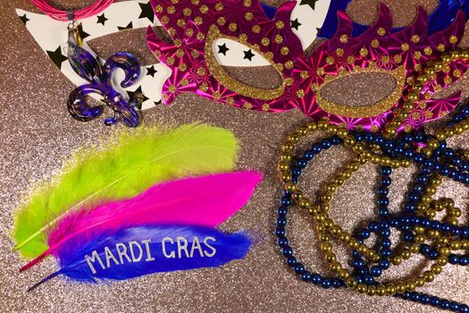 Mardi Gras carnival theme feathers and jewelry with party masks on textured gold surface layout