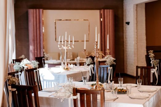 the presidium of the newlyweds in the banquet hall of the restaurant is decorated with candles and green plants, the general tone of the hall is beige