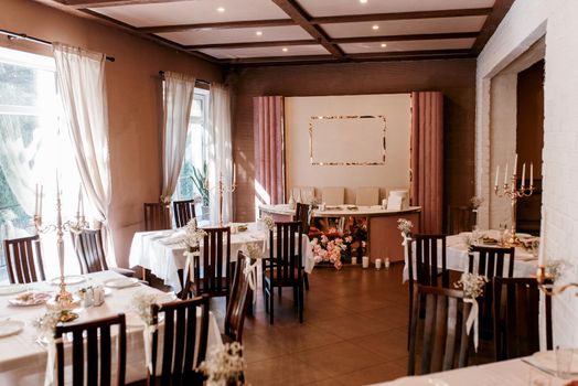 the presidium of the newlyweds in the banquet hall of the restaurant is decorated with candles and green plants, the general tone of the hall is beige