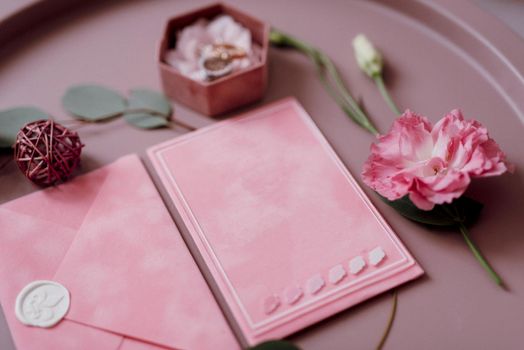 pink wedding invitation in a gray envelope on a table with green sprigs