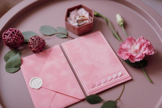 pink wedding invitation in a gray envelope on a table with green sprigs