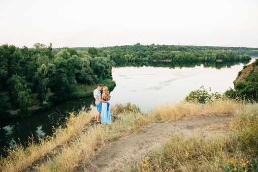 blonde girl with loose hair in a light blue dress and a guy in the light of sunset in nature