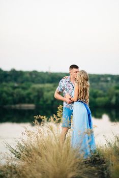 blonde girl with loose hair in a light blue dress and a guy in the light of sunset in nature