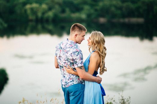 blonde girl with loose hair in a light blue dress and a guy in the light of sunset in nature