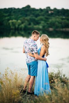 blonde girl with loose hair in a light blue dress and a guy in the light of sunset in nature