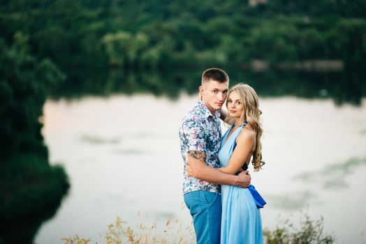 blonde girl with loose hair in a light blue dress and a guy in the light of sunset in nature