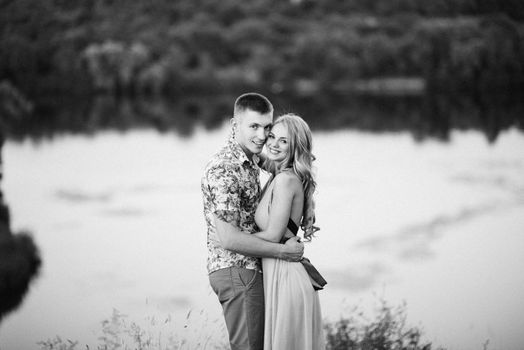 blonde girl with loose hair in a light blue dress and a guy in the light of sunset in nature