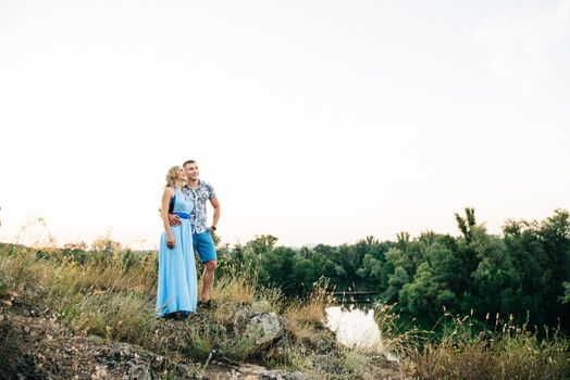 blonde girl with loose hair in a light blue dress and a guy in the light of sunset in nature