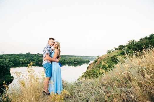 blonde girl with loose hair in a light blue dress and a guy in the light of sunset in nature