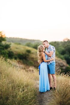 blonde girl with loose hair in a light blue dress and a guy in the light of sunset in nature