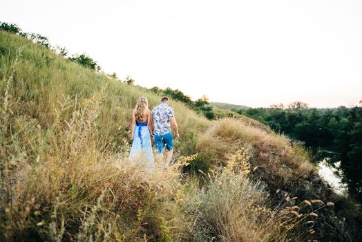 blonde girl with loose hair in a light blue dress and a guy in the light of sunset in nature