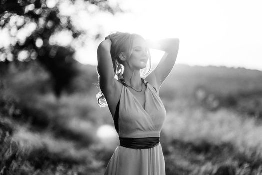 blonde with loose hair in a light blue dress in the light of sunset in nature