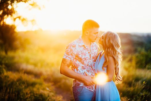 blonde girl with loose hair in a light blue dress and a guy in the light of sunset in nature